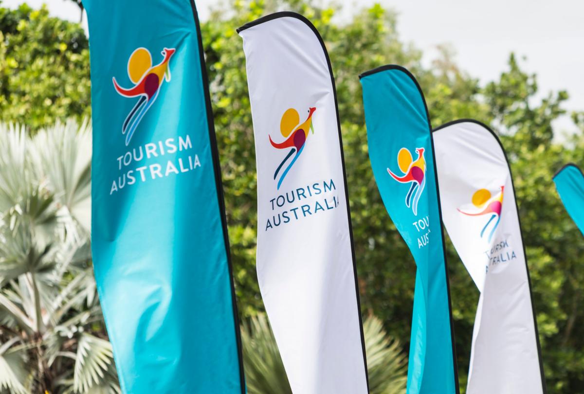 Against a backdrop of whispering palms and an endless canopy of green, the vibrant banners of Australia dance in the coastal breeze. The iconic kangaroo, splashed in the hues of a tropical sunset, sta